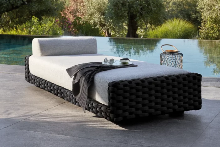 Low-profile black woven chaise lounge with thick white upholstery next to a pool