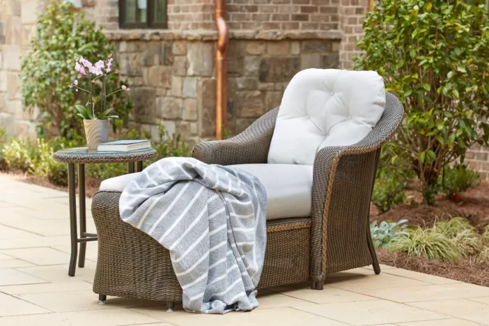 Dark brown all-weather wicker chaise with light grey upholstery and throw blanket