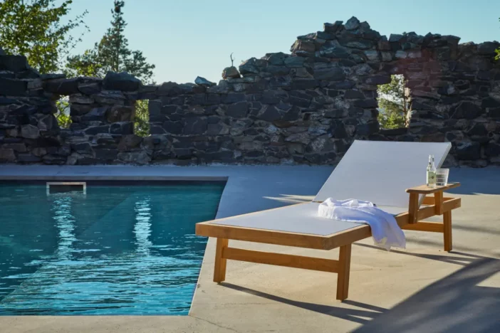 One-armed wooden sunlounger with white mesh sling on the side of a pool