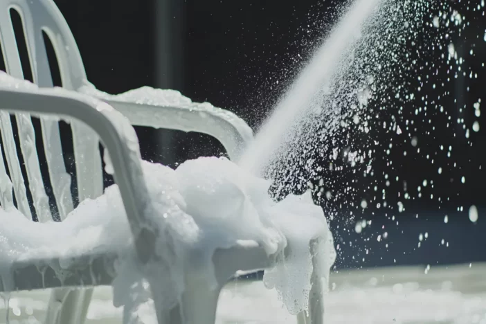 Close-up of white molded lawn armchair with soap suds and water spray