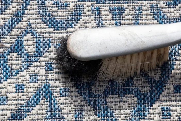 Close-up of a brush cleaning a blue and white patterned outdoor rug