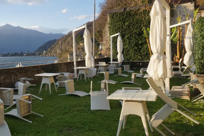 White wicker lawn chairs blown over by the wind on grass with closed umbrellas