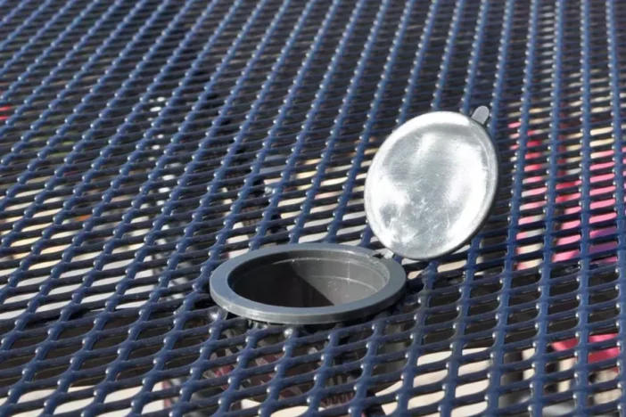 Close-up of black metal mesh tabletop with umbrella hole and plug