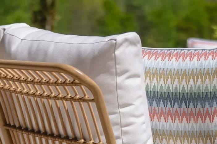 Back of a rattan outdoor sofa with white cushion and colorful patterned pillow