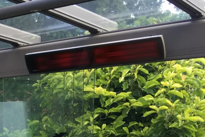 Modern electric outdoor heater mounted on a cross beam in a lush green setting