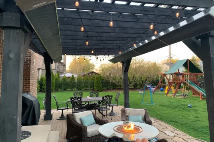 Grey wooden backyard pergola with long natural gas heaters mounted to the upper framework