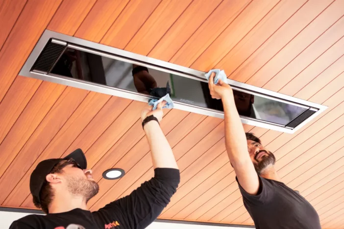 Two men installing a long modern electric patio heater in a wooden ceiling