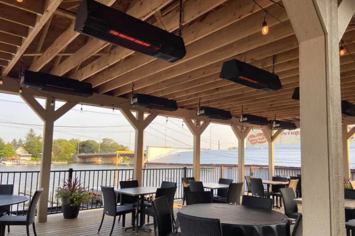 Black gas heaters suspended from wooden rafters over an outdoor dining area