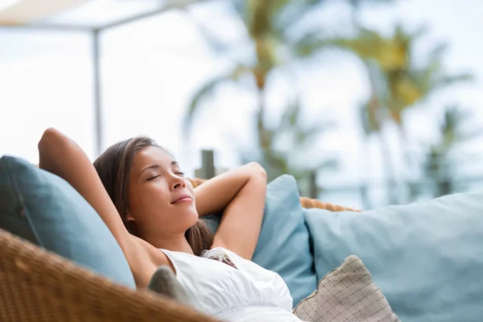Woman laying back in luxurious outdoor wicker sofa with blue pillows