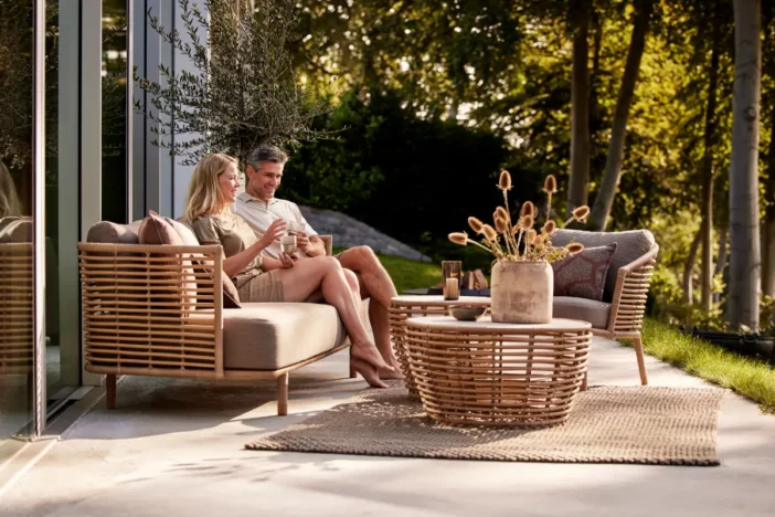 Couple sitting on a rattan outdoor sofa with matching lounge chair and tables
