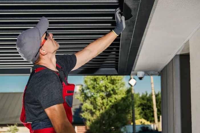 Technician in red overalls inspecting the louvers of a modern black pergola