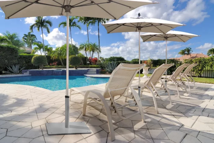 Three metal market umbrellas with fiberglass ribs and square white canopies shading sunloungers