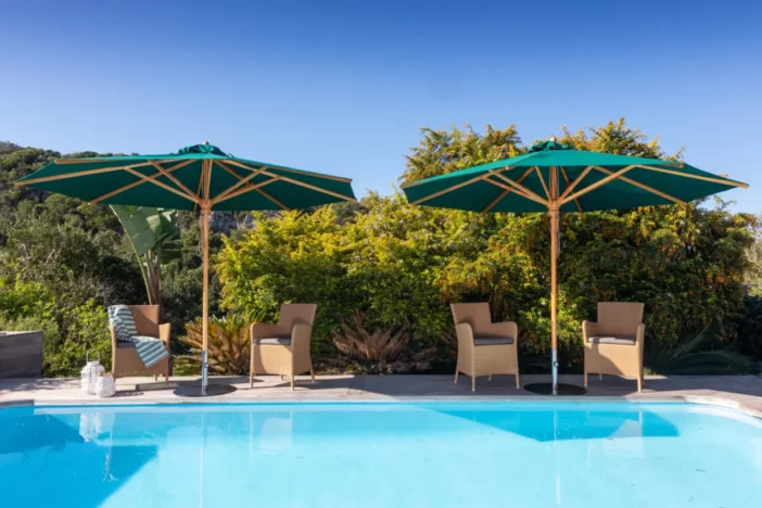 Wooden center pole umbrellas with octagon green canopies shading tan wicker armchairs poolside
