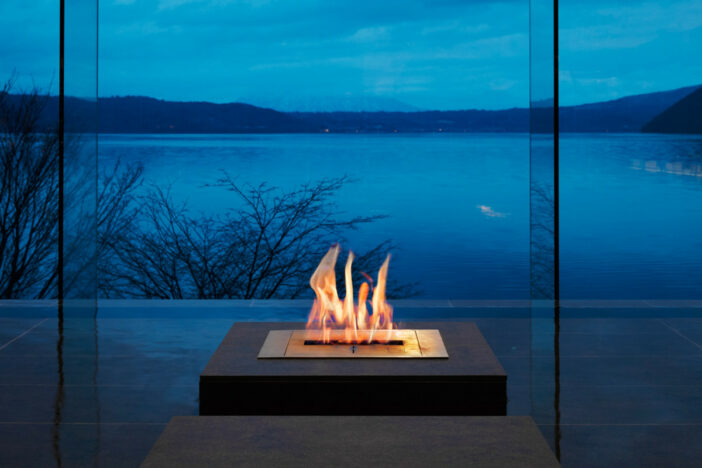 Square stainless steel EcoSmart Fire ethanol burner set into a concrete pedestal by a lake at dusk
