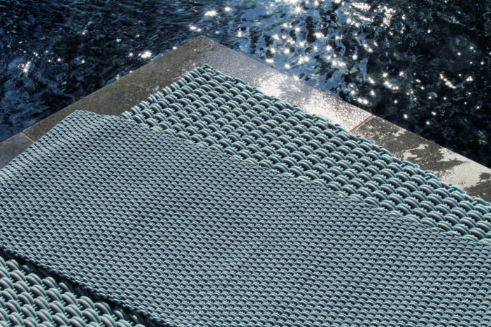 Two multicolored Shore outdoor rugs in aqua, teal, blue, and white beside a shimmering pool