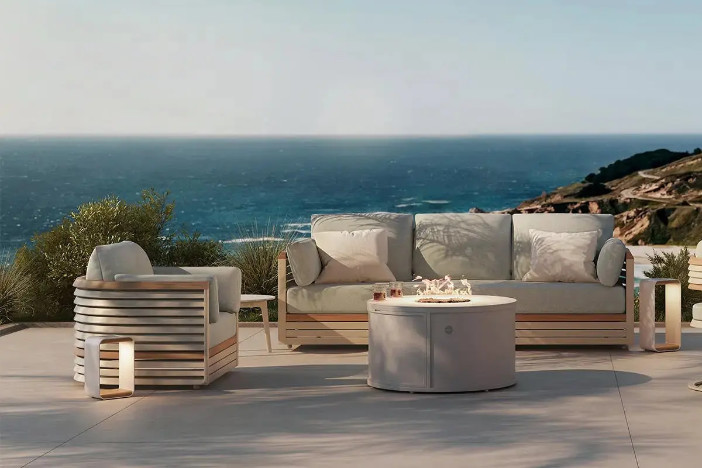 Modern beige and light brown wraparound lounge chair and sofa with light grey cushions around a fire pit on a seaside patio