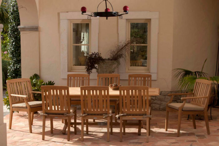 Classic teak outdoor dining table with matching vertical‑slatted chairs in a sunlit loggia