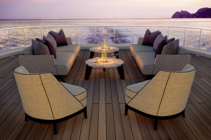Grey upholstered lounge chair and sofas with round candlelit coffee tables on the stern of a yacht