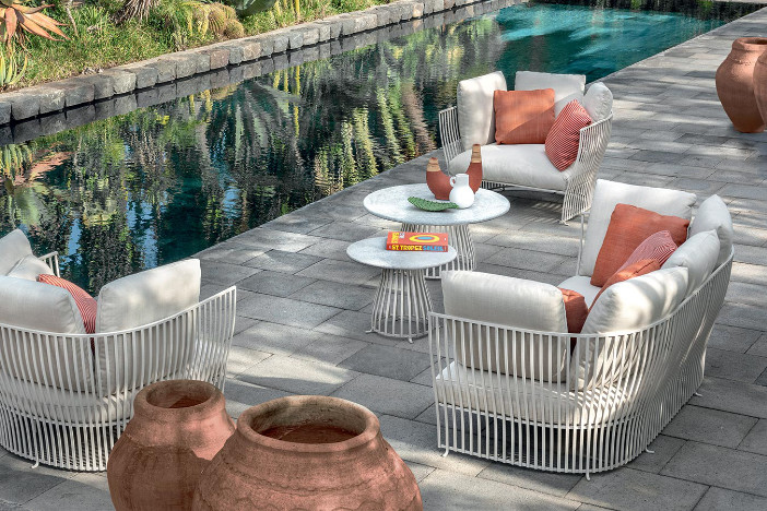Off‑white metal wireframe outdoor lounge set with plush cushions and muted melon accent pillows on a concrete poolside patio