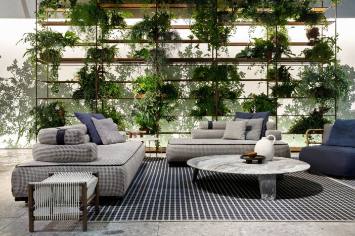 Neatly upholstered blue and white low‑profile sectional pieces on a covered patio with a wall of potted plants