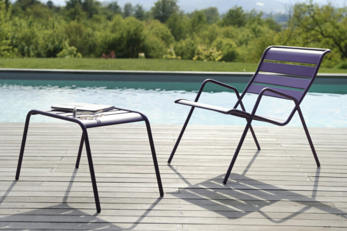 Minimalist purple tubular metal lounge chair and ottoman with wide slats on a poolside deck