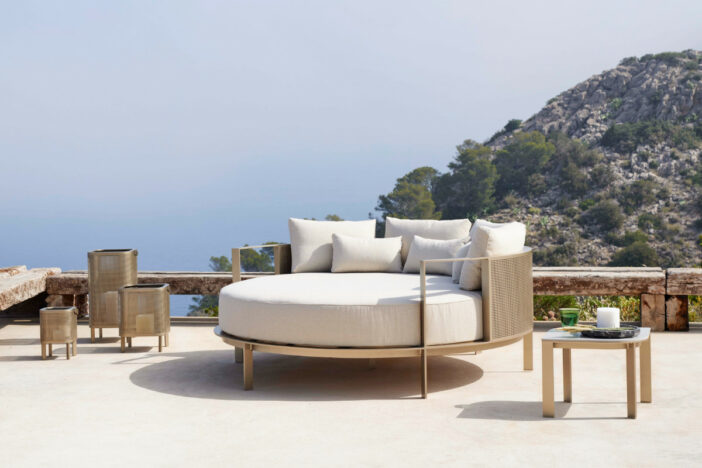 Elegant round outdoor daybed with perforated golden metal frame and off‑white cushion and pillows on a Mediterranean terrace