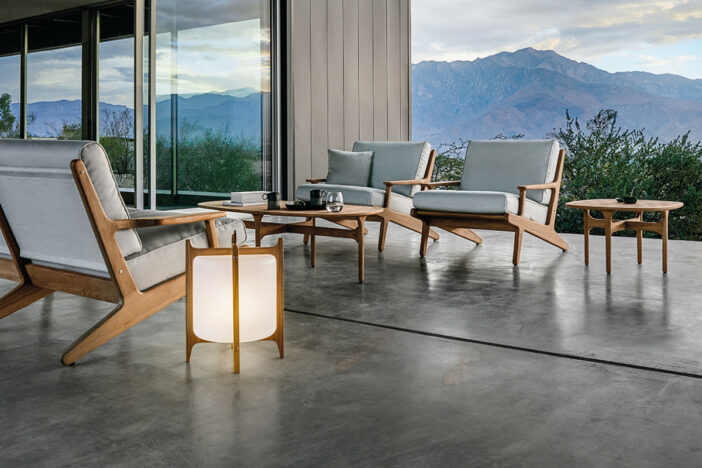 Angular contemporary teak lounge chairs with light grey cushions and matching tables and floor lamp on a smooth patio with a mountain backdrop