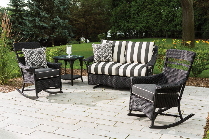 Traditional black outdoor wicker rocking chairs and loveseat with black and white cushions on a small garden patio