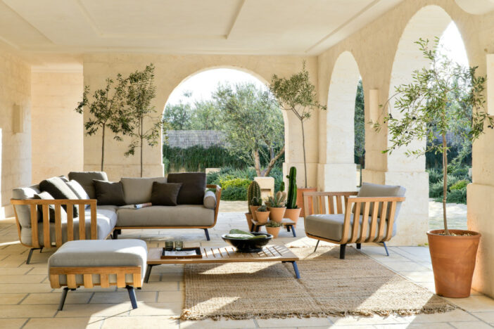 Modern bentwood slat‑framed lounge seating and low table with potted plants in an arched loggia