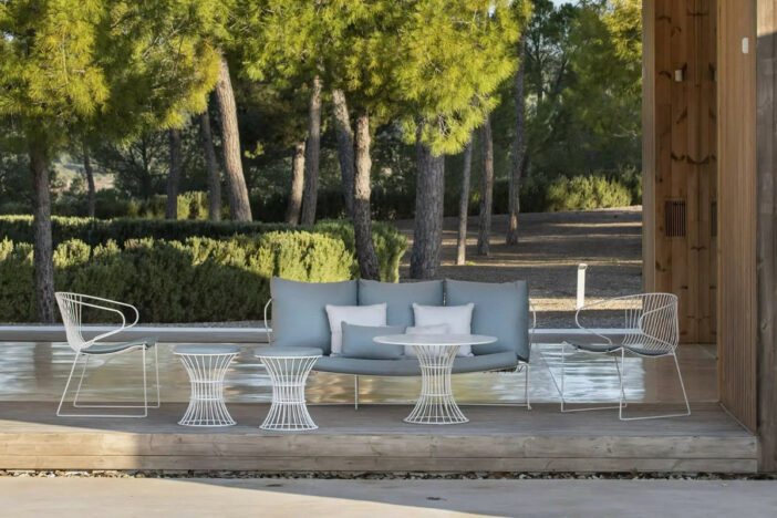White wireframe lounge set with curved design and grey cushions on a covered patio in the woods