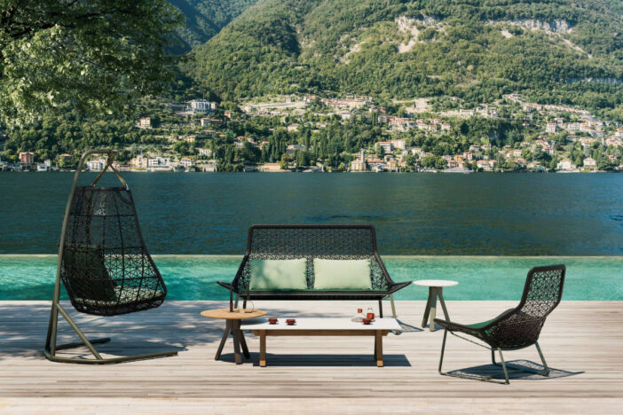 Geometric black open‑weave lounge chair, sofa, and hanging seat on a lakeside deck