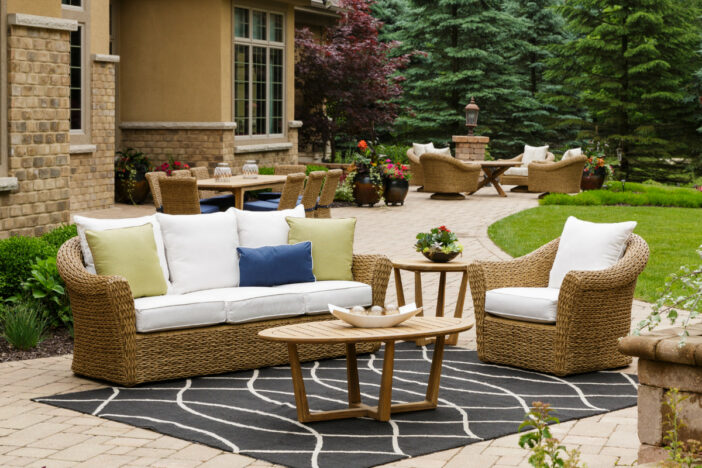 Honey brown minimalist wicker lounge and dining sets on a spacious wraparound patio in a wooded setting