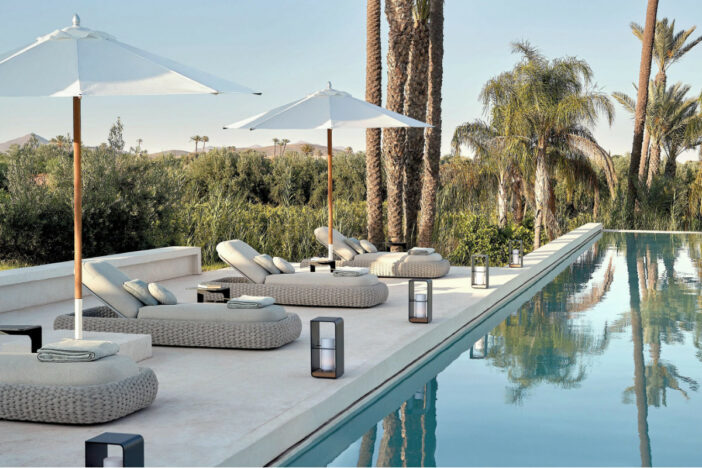 Minimal modern white wicker sunloungers with rounded forms, thick off‑white cushions, and market umbrellas in a tropical poolside setting