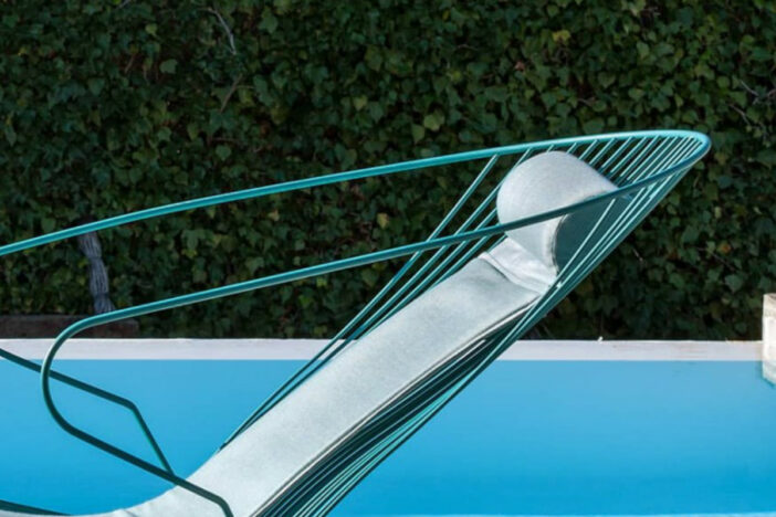 Close‑up of the head of a vibrant teal wireframe sunlounger with thin seafoam back cushion and headrest beside a pool