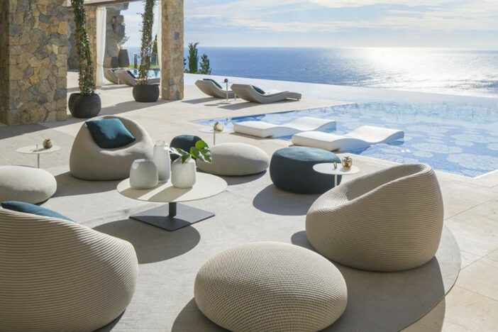 Minimalist pebble‑like off‑white woven lounge pieces with turquoise pillows on a spacious patio with a seaside view