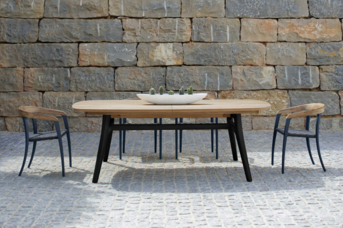 Two‑tone wooden outdoor dining set with curving black frames, natural woodgrain tabletop, and wraparound backrests on a stone‑walled patio