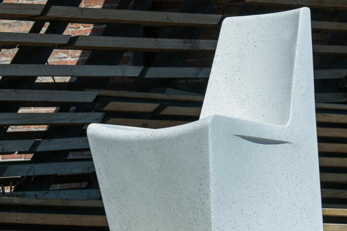 Close‑up of a white mineral outdoor chair with angular backrest and scoop seat against dark horizontal wood slats
