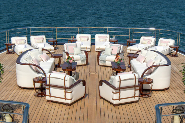 Bespoke white upholstered lounge seating and sunloungers on the hardwood deck of a large yacht