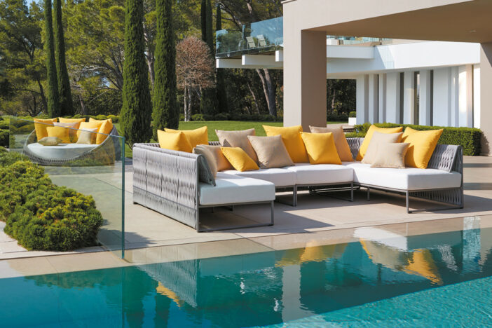 Modern outdoor sectional with beige‑grey woven polyester backs, thick white cushions, and yellow accent pillows on a poolside patio