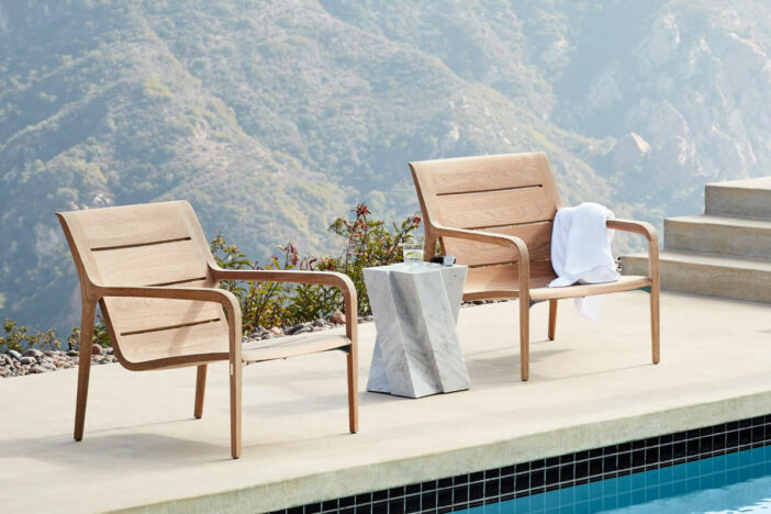 Sculpted teak lounge chairs with curving wide slat seats and narrow legs on a concrete poolside with mountain views