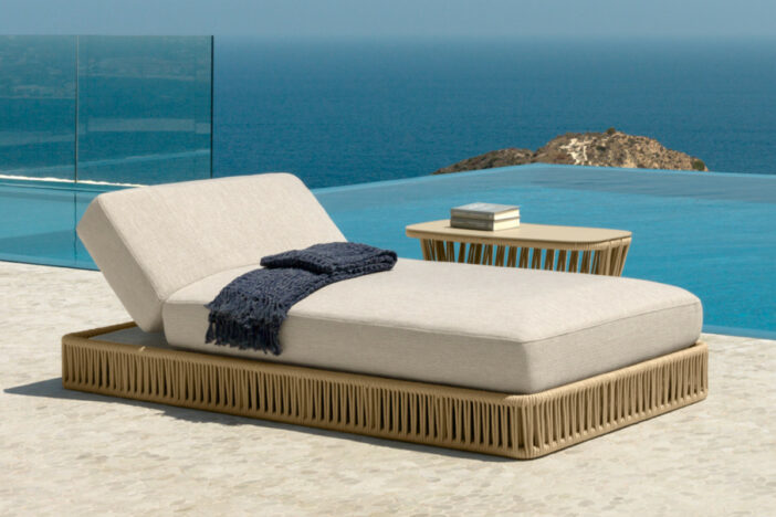 Low‑profile platform sunlounger with tan rope wrap and thick adjustable off‑white cushion beside an infinity pool