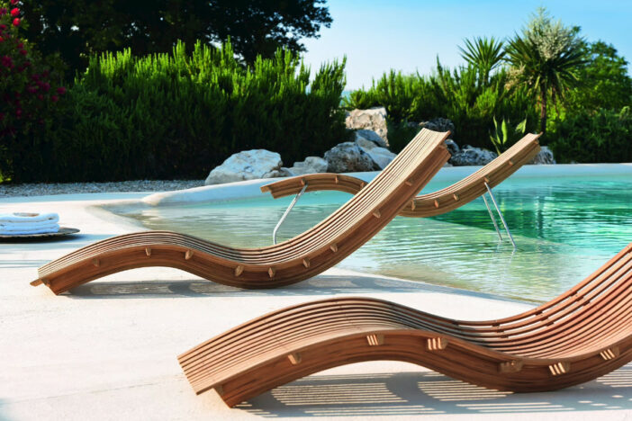 Three minimalist teak slat sunloungers with S‑curve designs lined up on a small inlet beach