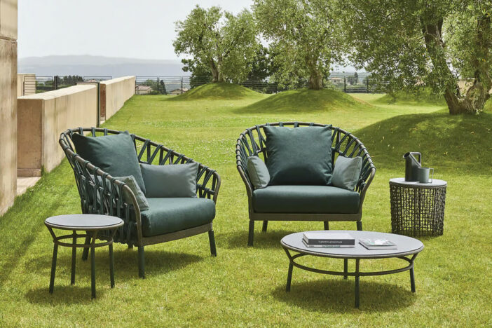 Wide wraparound outdoor lounge chairs with forest green criss‑cross synthetic straps and matching cushions with low tables on grass