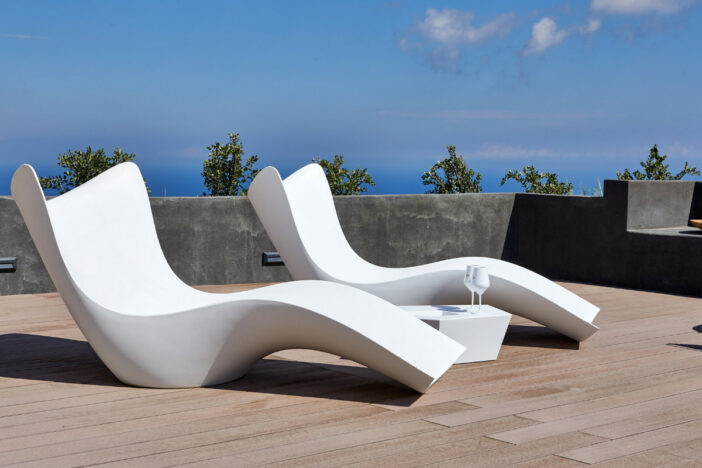 Sculpted white plastic sunloungers with flowing lines on a wooden deck