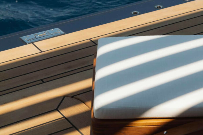 Close‑up of the foot of a sunlounger with glossy marine‑finished teak base and white cushion at the edge of a yacht deck