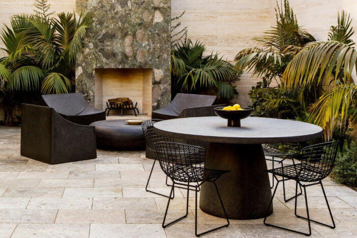 Sculpted minimalist black metal outdoor lounge chairs and dining set near an outdoor fireplace on a stone paver patio
