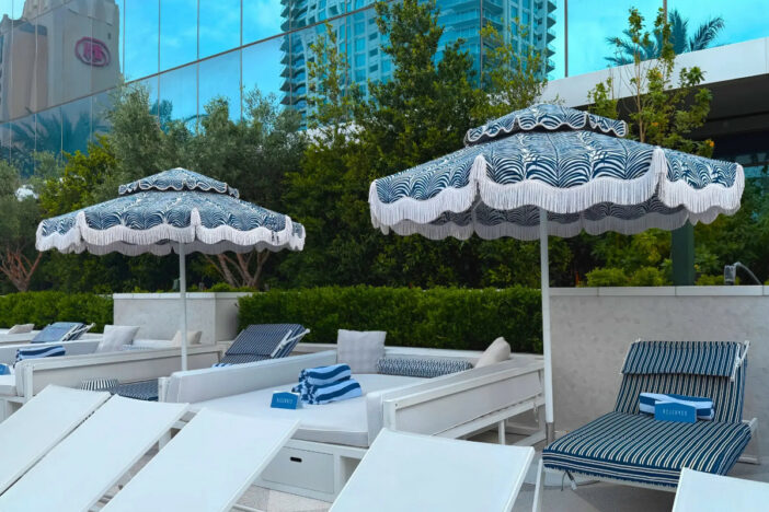 Two Poggesi center‑pole umbrellas with teal and white valanced canopies shading hotel pool seating
