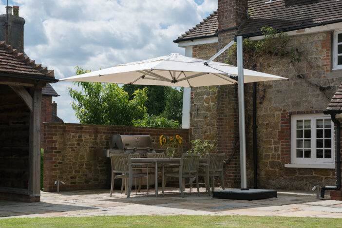 Silver‑frame Shademaker cantilever umbrella with off‑white canopy shading a small outdoor dining set