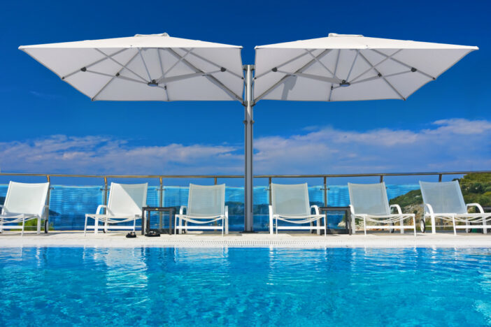 Modern dual white Shadowspec cantilever canopies shading rows of sunloungers beside a bright blue pool