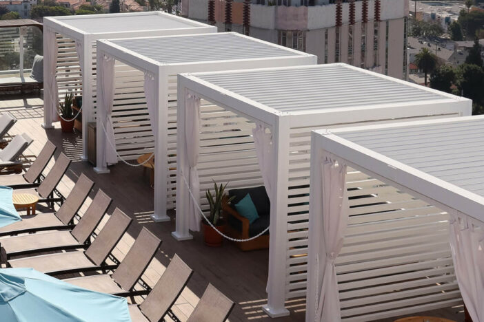 White StruXure pergola‑roof cabanas with curtains around a rooftop swimming pool